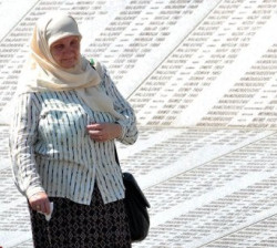 Unha bosn&iacute;aca musulm&aacute; cami&ntilde;a ao car&oacute;n do muro memorial do Cemiterio de Srebrenica